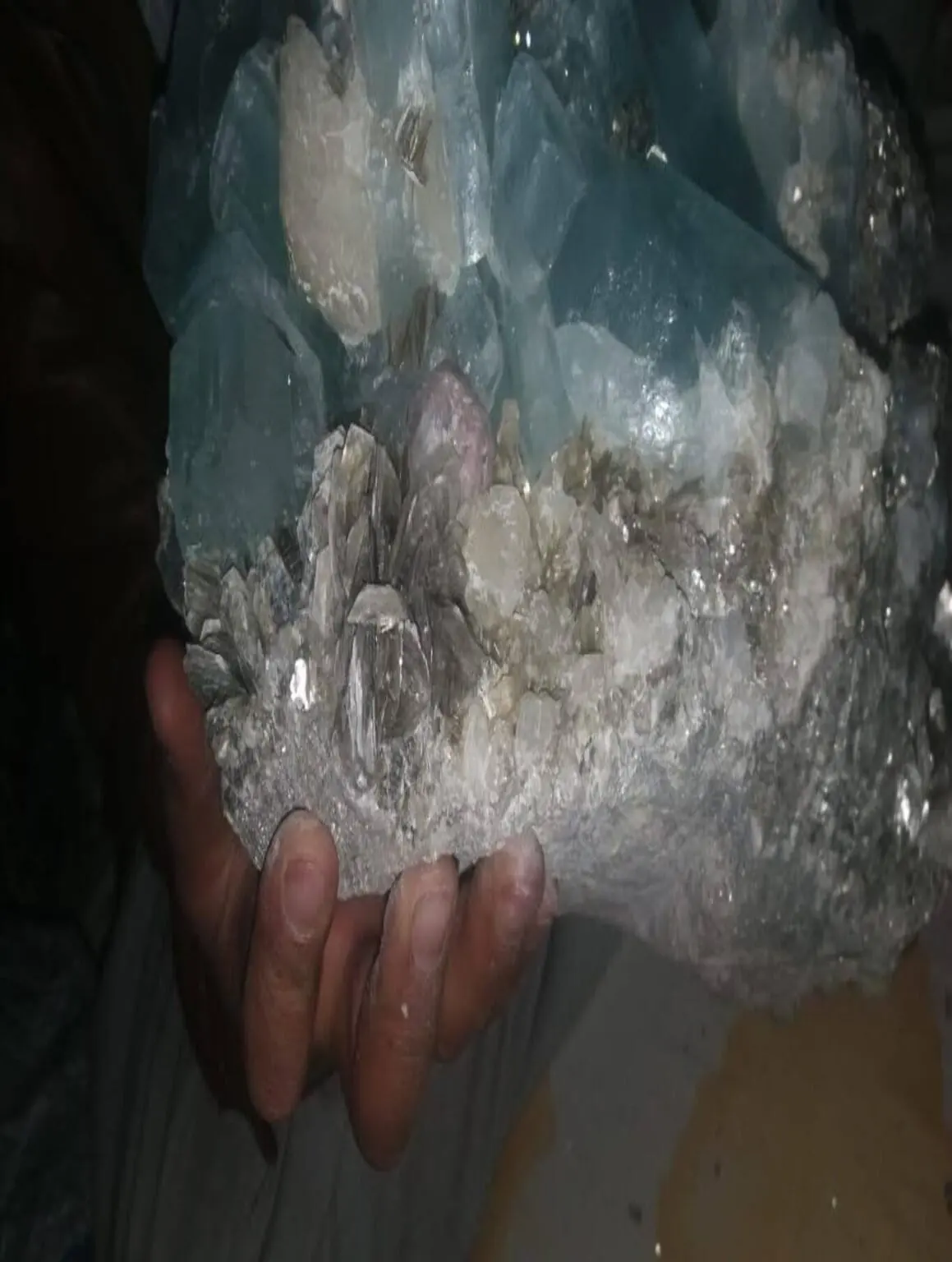 A large aquamarine crystal cluster on matrix held in hand