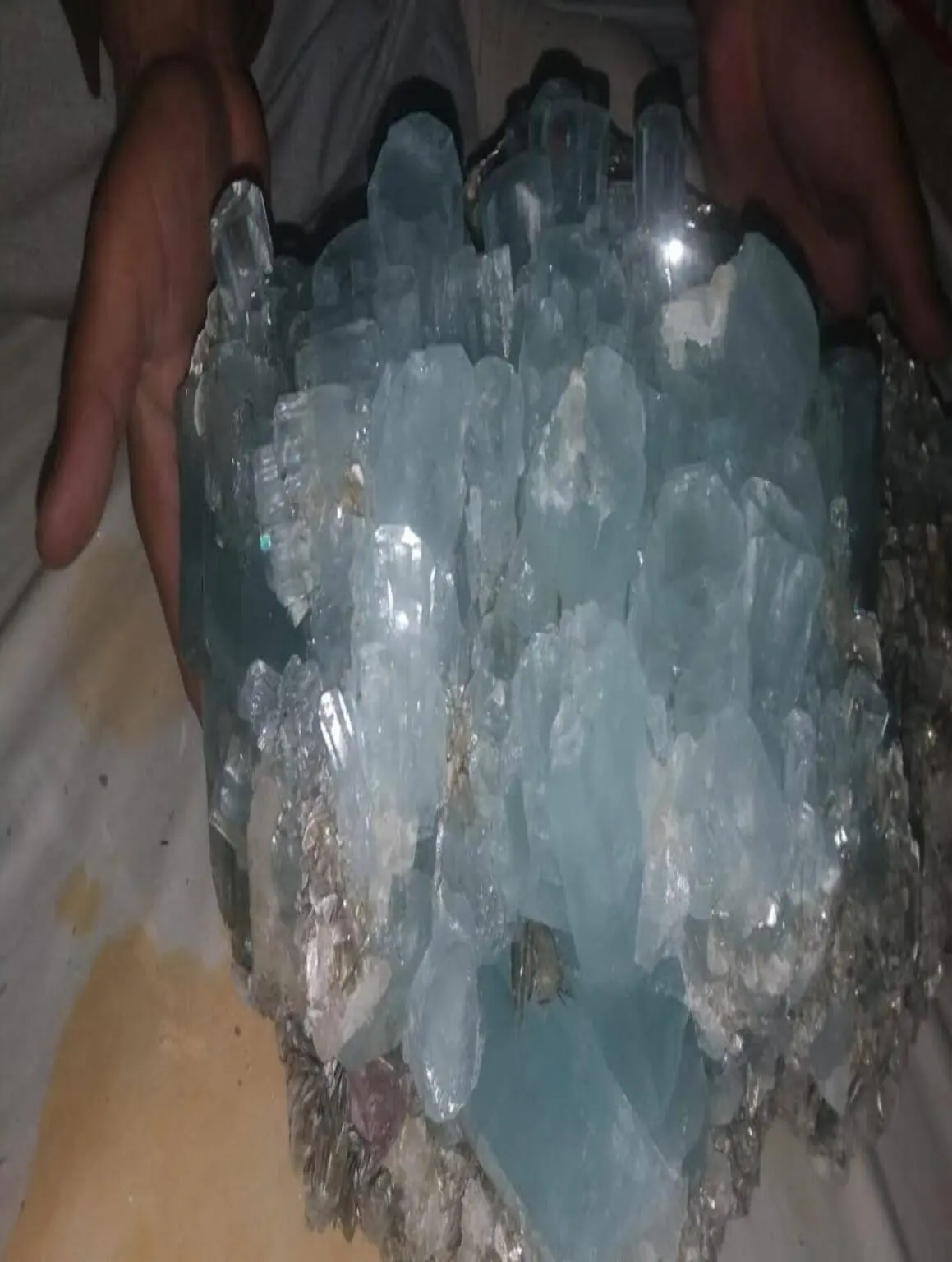 A large aquamarine crystal cluster held with two hands