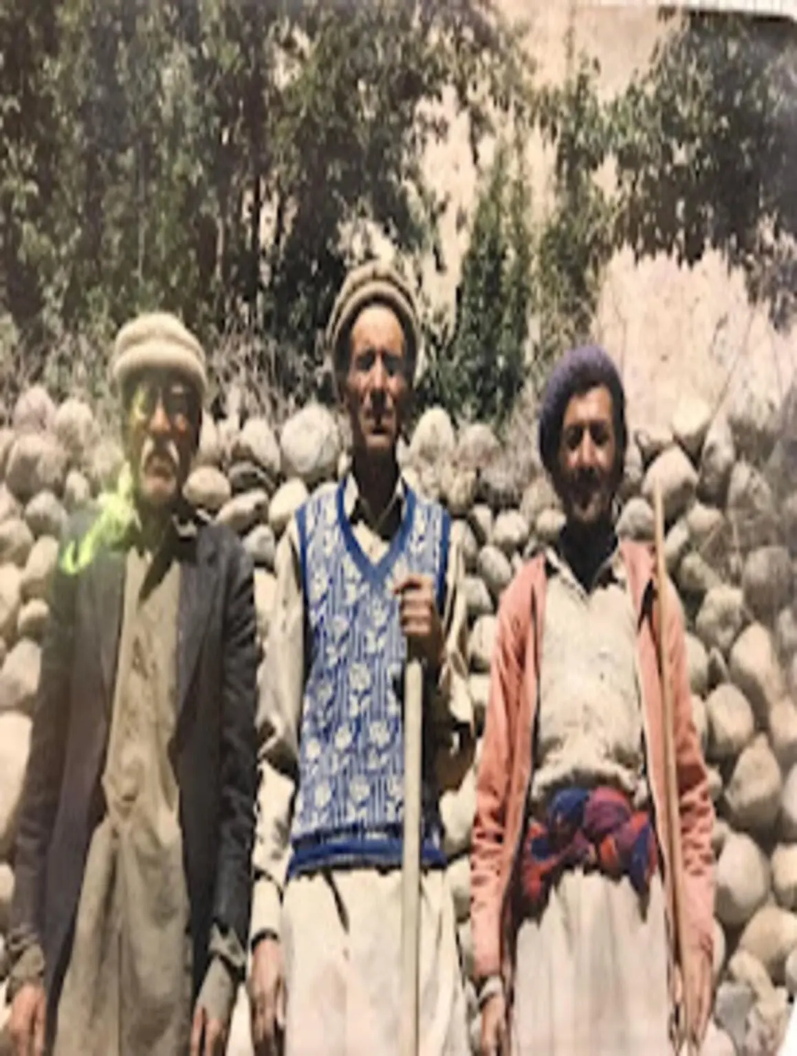 An archival tinted photograph of three men standing by a riverbed with walking sticks