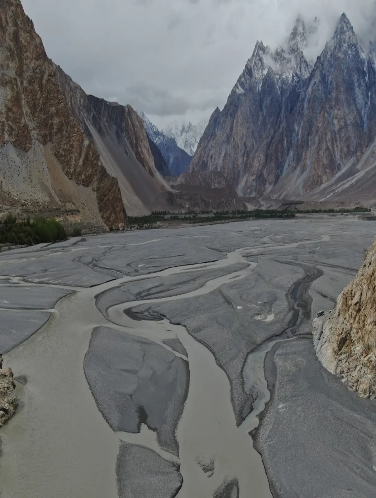Wide view of a braided glacial river valley beneath the Passu Cones