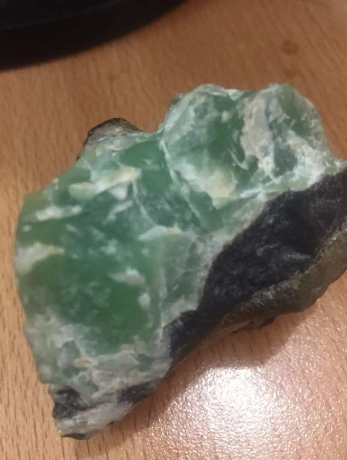 A raw green mineral specimen with dark host rock
