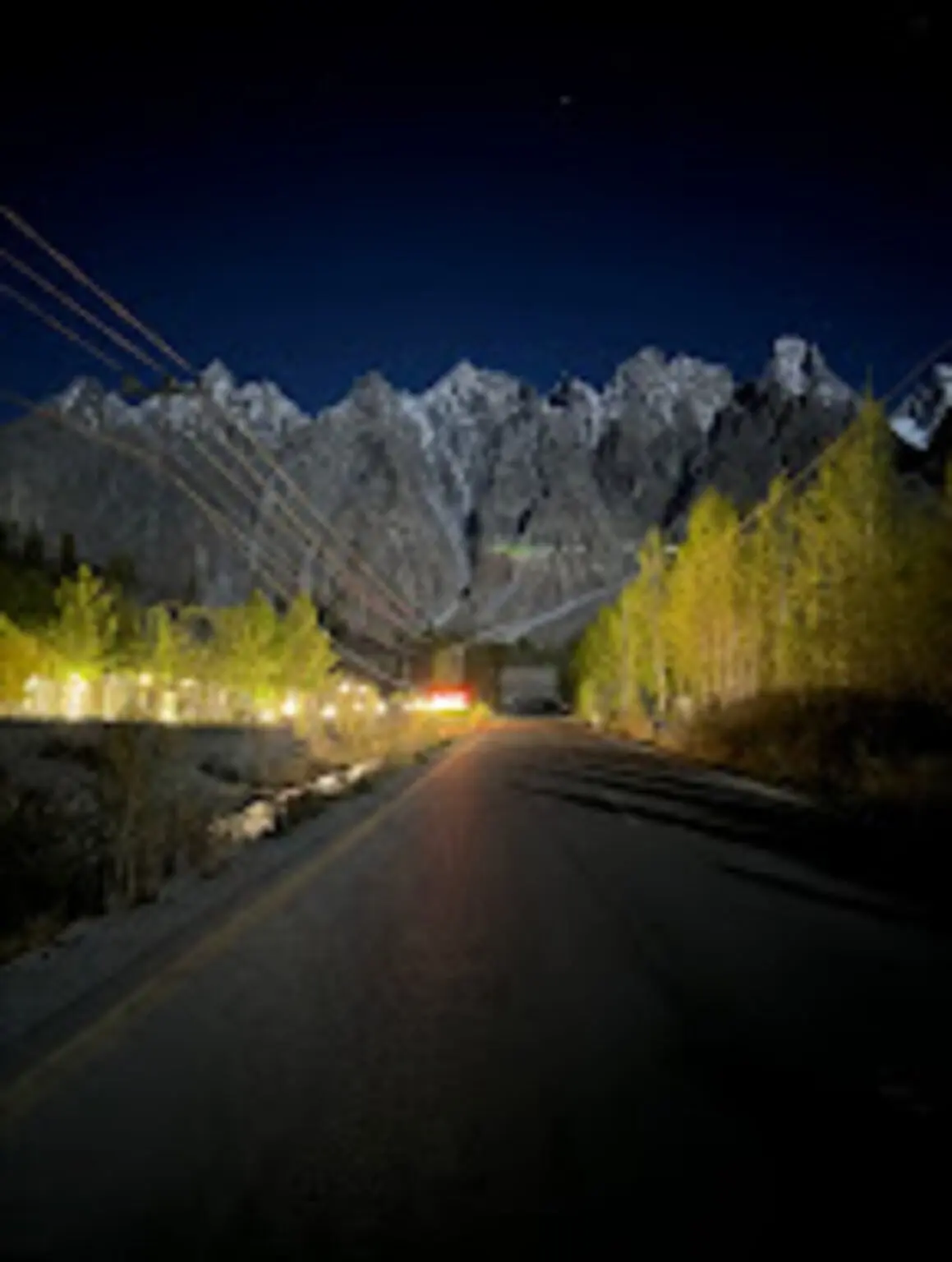 A mountain road at night lit by streetlights, with peaks visible under starlight
