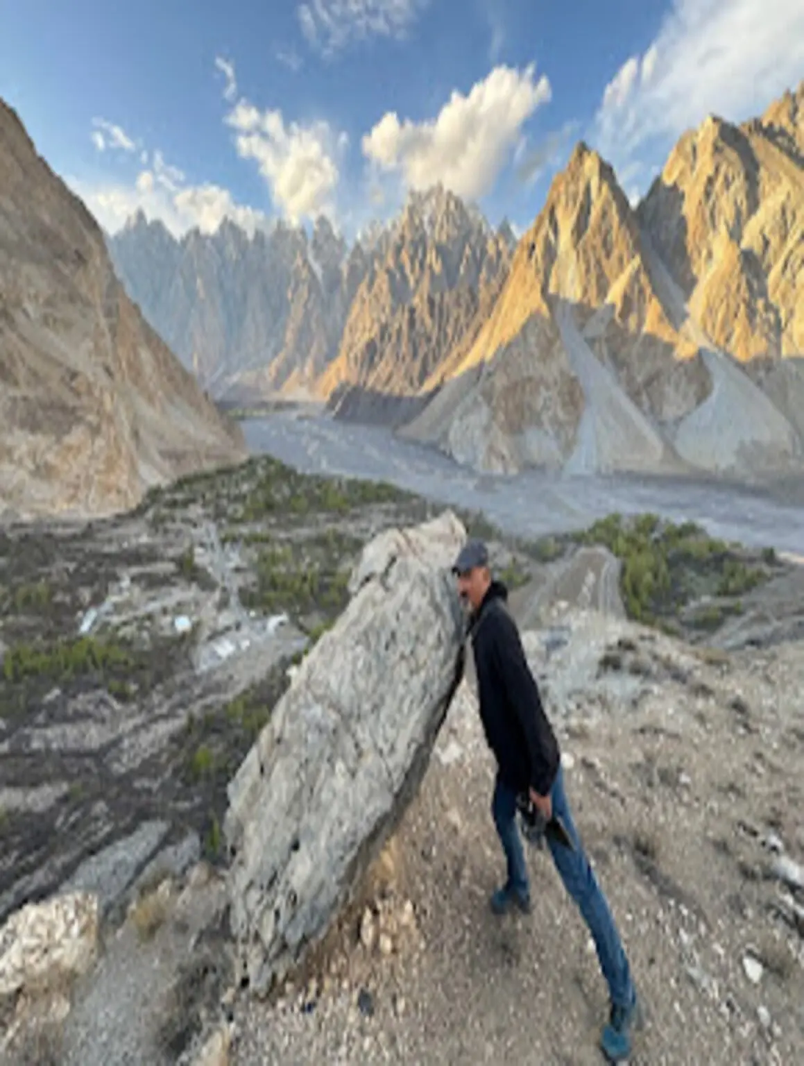 A man leaning on a large rock overlooking the Passu Cones and river valley below